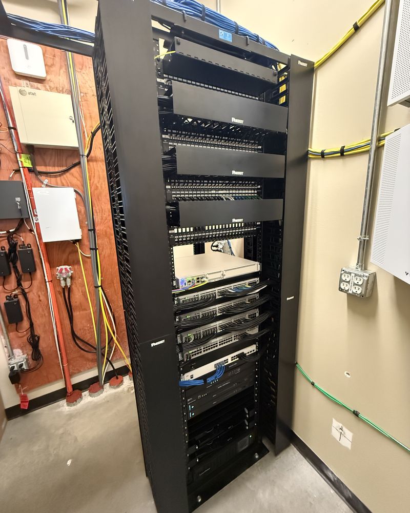 A floor-to-ceiling distribution rack: patch panels landed and dressed above, switching below, service demarcation on the wall alongside.