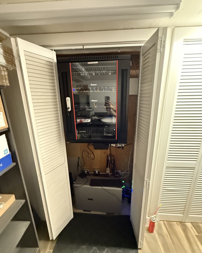 A wall-mounted enclosed rack in a utility closet, with patch panels, switching, and a rack-mounted UPS